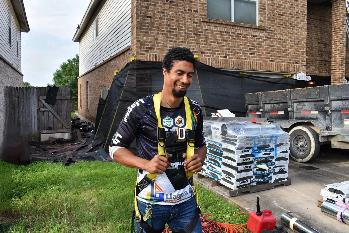Llagua Roofing professional adjusting safety harness beside shingles and equipment at a residential roof job site