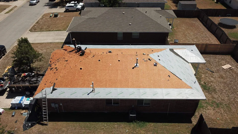 A Llagua Roofing crew installing architectural shingles over orange synthetic underlayment on a home in Leander, Texas